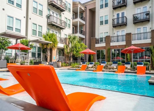 a swimming pool with orange chairs in front of an apartment building