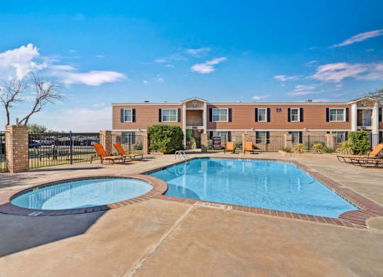 A refreshing outdoor swimming pool here at Golden Crest with clear blue water, a spacious concrete deck, and surrounding lounge chairs, featuring a separate shallow pool area and a fenced courtyard setting under bright, sunny skies.