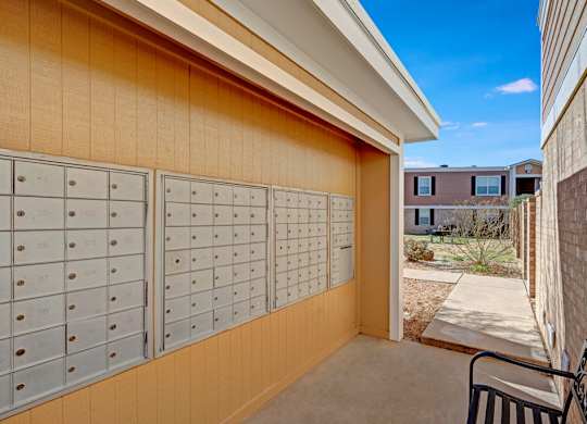 A covered community mailbox area here at Golden Crest with neatly organized mailboxes, neutral-toned siding, and a shaded walkway that leads into the landscaped courtyard, offering a convenient and accessible mail pickup space.