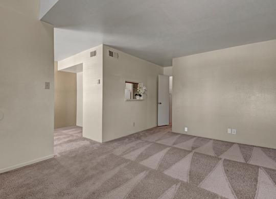 A spacious, empty living room here at High Plains with soft beige carpet, neutral walls, and an open layout, featuring a pass-through window to the kitchen and multiple wall openings that create a bright, flexible space for everyday living.