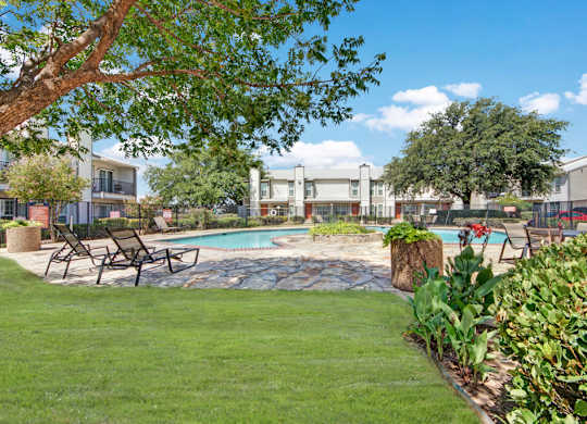 A resort-style outdoor pool area here at High Plains with a sparkling swimming pool, lounge chairs, and a stone pool deck surrounded by lush green landscaping. Mature trees provide shade, and nearby apartment buildings create a calm, inviting community atmosphere.