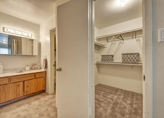 A convenient bathroom and closet area here at High Plains with a wooden vanity and light countertop, a mirrored medicine cabinet with overhead lighting, and an adjacent walk-in closet with shelving, offering a functional and organized layout.