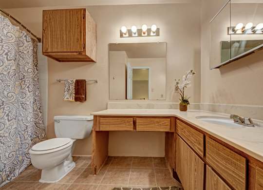 A spacious bathroom here at High Plains with a large wooden vanity, light countertops, and dual sink areas, featuring a bathtub-shower combo, ample cabinet storage, and bright lighting for a comfortable and functional space.