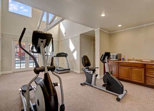 A well-equipped fitness center here at Las Colinas with cardio machines, including treadmills and stationary bikes, set on plush carpeting. Large windows and bright lighting create an open, energizing space, with a convenient counter area adding comfort for residents during workouts.