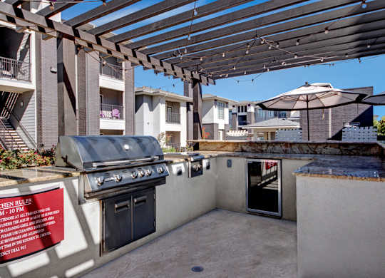 A BBQ grill is on a patio with a sign that says "Kitchen Rules".