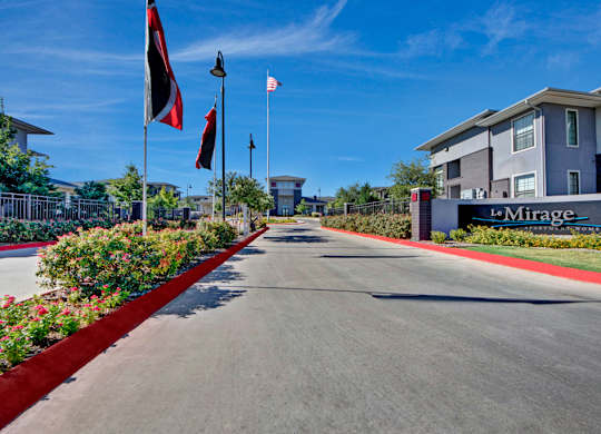 A street view of Le Mirage with flags on poles and a building on the right.