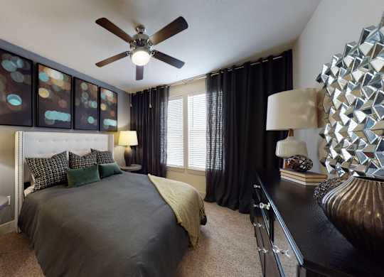 A bedroom with a bed, a ceiling fan, and a side table with a lamp.