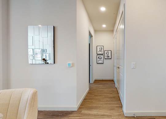 A bright interior hallway here at Magnolia on the Green with wood-style flooring, recessed ceiling lights, white doors, and modern wall art, creating a clean and welcoming passage between rooms.
