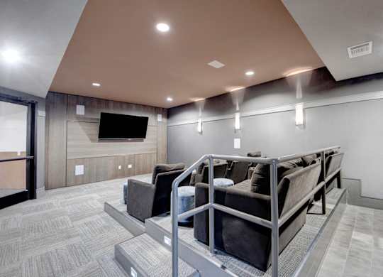 A media room here at Sorrel Fairview with tiered theater seating, dark gray lounge chairs, wall-mounted TV, wood accent wall, and soft recessed lighting for a cozy viewing space.