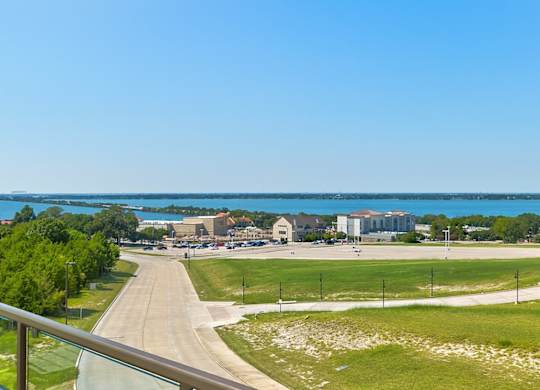 A balcony view here at Sorrel Fairview overlooking a wide green lawn, curving road, and bright blue lake in the distance under clear sunny skies.