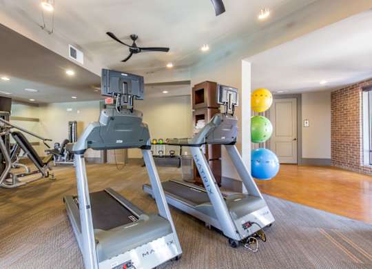 A fitness center here at Sorrel Fairview with modern treadmills, strength machines, free weights, colorful exercise balls, track lighting, and warm wood-tone floors in a bright, spacious workout room.