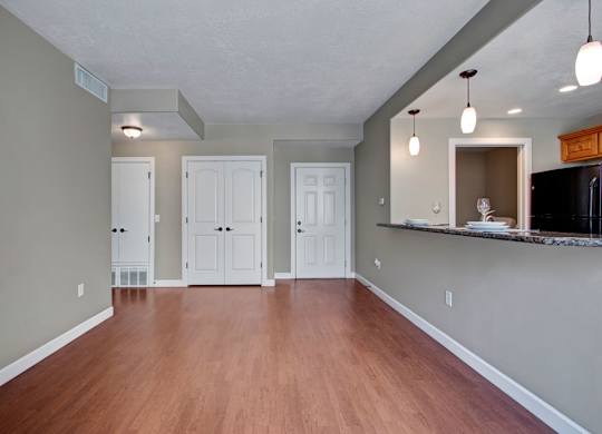A living and dining area here at Bridges with warm wood flooring, soft gray walls, white double-door closet, entry door, and a granite breakfast bar with pendant lights and place settings.