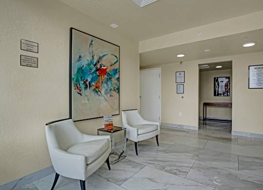 Two white chairs are placed in front of a painting in a hallway.