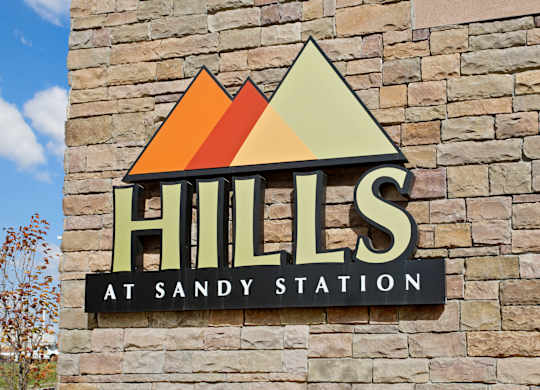 A sign that says Hills at Sandy Station is mounted on a stone wall.