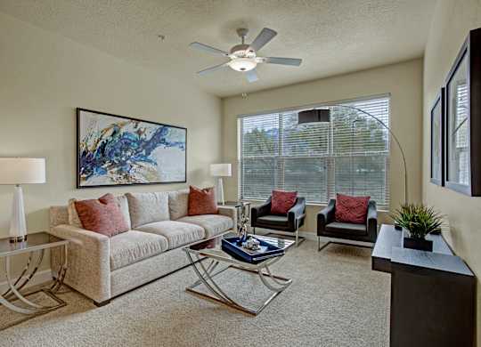 A living room with a couch, two chairs, a coffee table, and a ceiling fan.