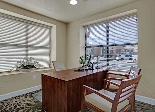 A room with a desk and a chair in front of a window with blinds.