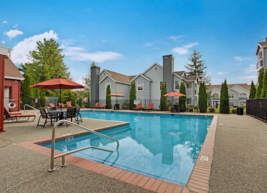 A swimming pool surrounded by a patio with chairs and umbrellas.