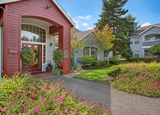A red house with a white door and windows is surrounded by a garden with pink flowers.