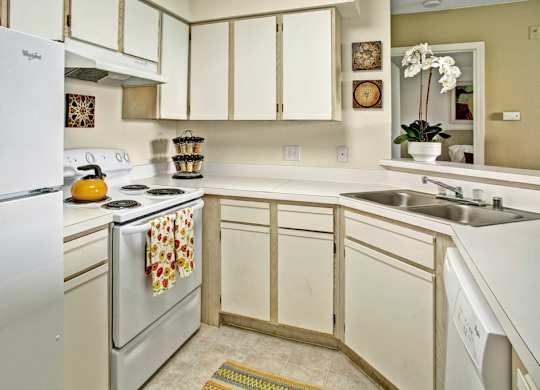 A white refrigerator is in a kitchen with a white stove and white cabinets.