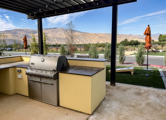 an outdoor kitchen with a grill and a table with umbrellas in the background
