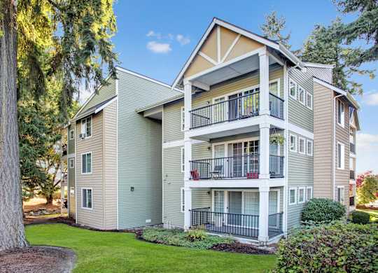 A large apartment building with a balcony and a tree in front.
