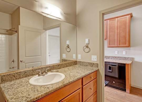 A bright bathroom here at Riverside 9 with granite countertop vanity, large mirror, and convenient access to in-home laundry area.