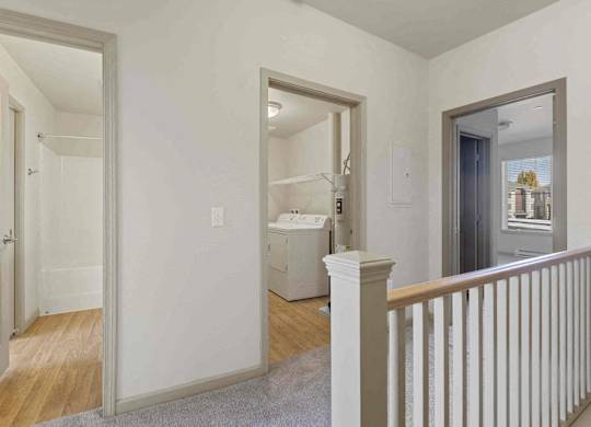 A convenient hallway here at Riverside 9 with in-home laundry closet, nearby bathroom access, and soft carpet flooring leading to bright bedrooms.