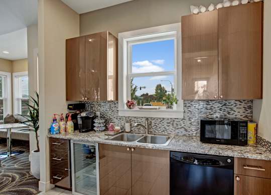 A convenient community kitchen here at Riverside 9 with modern cabinets, granite countertops, mosaic backsplash, sink, and beverage appliances in a bright, welcoming space.