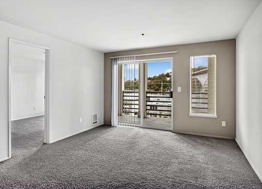 A room with a carpeted floor and a view of a balcony through a glass door.