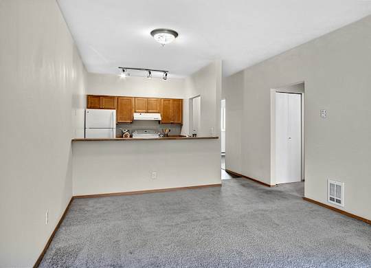 Empty room with a kitchen area in the background.
