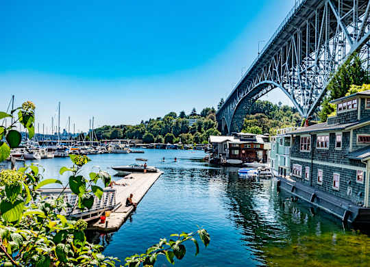 A bridge spans across a calm body of water with houses on the right and boats in the distance.