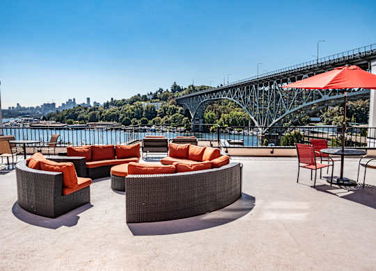 A patio with orange cushions and a view of a bridge and city skyline.