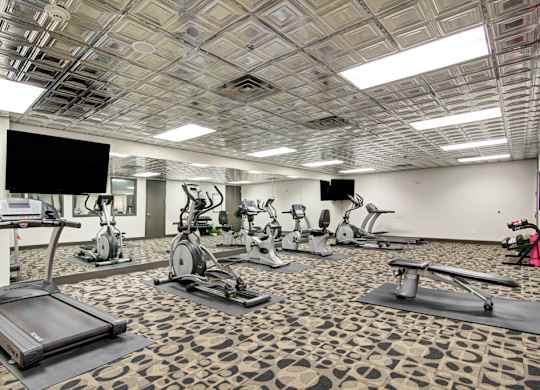 A gym with treadmills, exercise bikes, and a television.