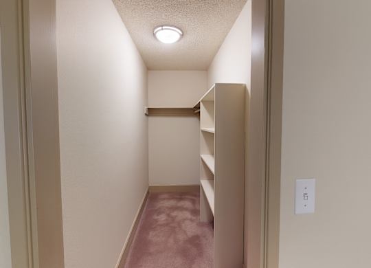 A spacious walk-in closet here at Whispering Cedars with soft carpet, built-in shelving, and a hanging rod, offering ample storage space and an organized layout for comfortable, convenient living.