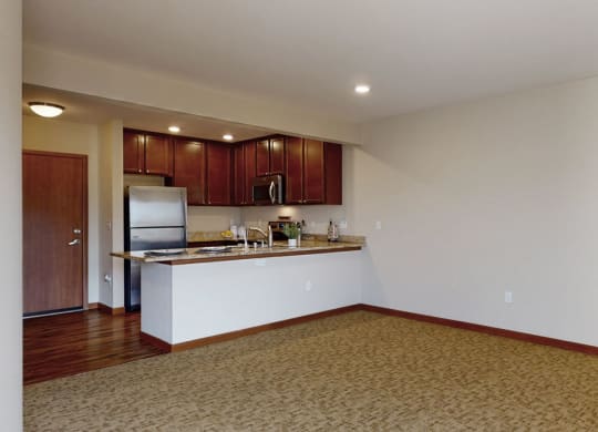 an empty living room with a kitchen in the background