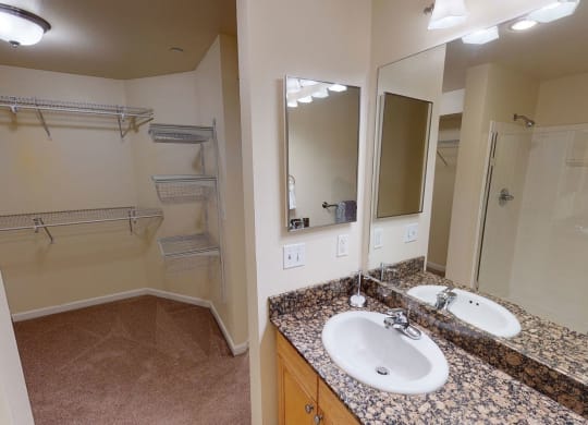 Spacious Admirals Cove Apartment bathroom with granite countertop and sink, large mirror, and walk-in closet. Shower with glass door. Modern, clean, and well-lit.