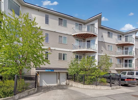 Admirals Cove four-story apartment building with white siding and glass balconies under a clear sky. Green trees and parked cars are in the foreground.