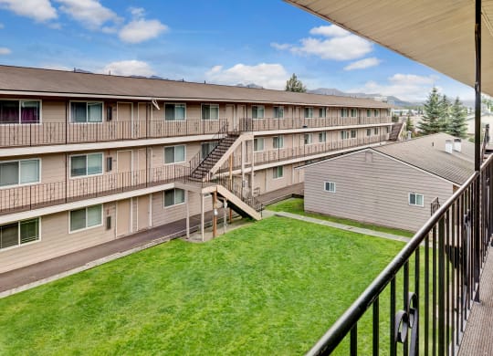 College View Apartment complex with three stories, beige siding, and black railings. A green courtyard is visible below, under a partly cloudy blue sky.
