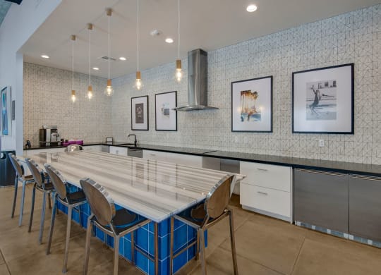 Modern kitchen here at Roosevelt Row Apartments with sleek design, featuring a marble island, metallic chairs, pendant lights, and framed art on a patterned wall. A clean, elegant ambiance.