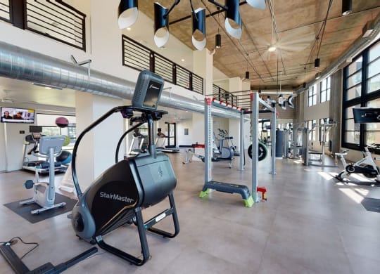 Spacious modern gym here at Roosevelt Row Apartments with large windows and natural light. It features a StairMaster, exercise bikes, treadmills, free weights, and sleek ductwork.