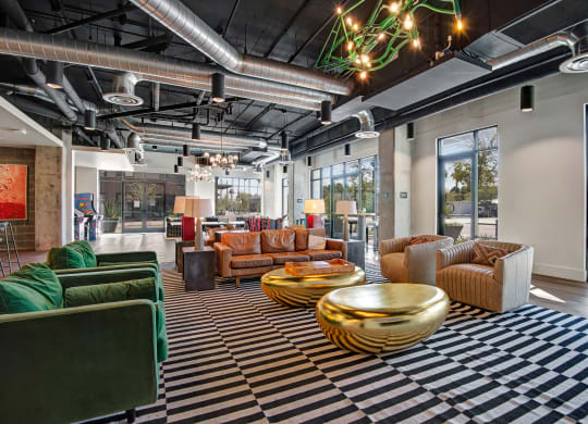 Modern lounge here at Roosevelt Row Apartments with striped carpet, leather and green velvet sofas, gold coffee tables, and exposed ductwork. Bright, airy, and stylish ambiance.