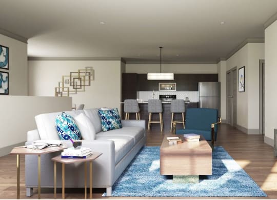 Modern living room here at 49 West Apartments with a gray sofa and colorful pillows, blue accent chair, and wooden coffee table on a blue rug. Stylish kitchen in the background. Bright, airy vibe.
