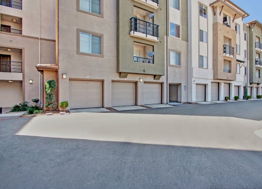 Modern Artisan at Main Street Metro Apartment complex with beige and olive exteriors. Features multiple balconies, closed garages, and small plants, creating an urban, tidy atmosphere.