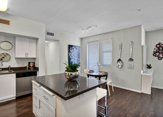 Modern kitchen and dining area here at Artisan at Main Street Metro Apartments with dark wood floors, white cabinets, and a gray countertop island. Wall decor includes oversized silver utensils.