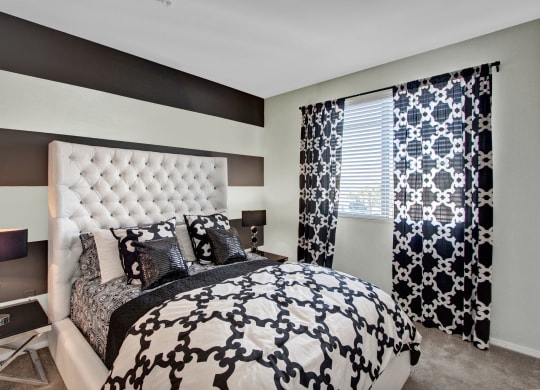Sophisticated bedroom here at Artisan at Main Street Metro Apartments with gray and white striped walls, a tufted headboard, and matching patterned bedding and curtains. Two modern lamps add elegance.