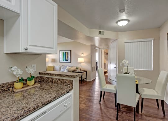 Modern open-plan dining and living area here at Castlepark Apartment Homes with warm, neutral tones. Features a round table with white chairs, cozy living room, and a granite countertop.