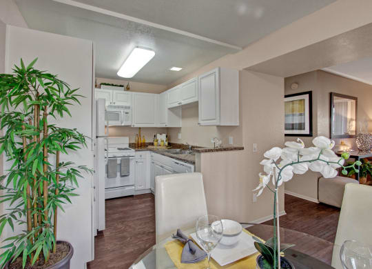 Modern kitchen and dining area here at Castlepark Apartment Homes. White cabinets, granite countertops, and appliances in the kitchen. Dining table with orchids and elegant table setting, exuding a cozy, welcoming atmosphere.