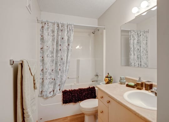 Bathroom here at Edgewood Estates Apartment Homes with a floral shower curtain, beige walls, and a wooden vanity with a sink. A mirror reflects light from above, creating a cozy ambiance.