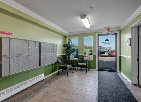 Edgewood Estates Apartment Homes lobby with pale green walls, a wall of mailboxes, and wicker chairs around a small table featuring a plant. A glass door leads outside.