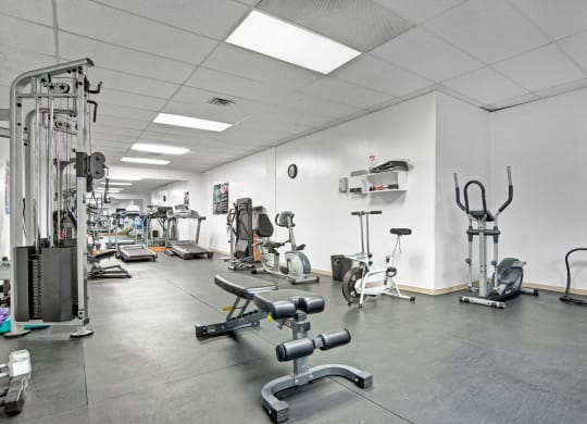 Gym interior here at Marquis Towers Apartment Homes with various exercise equipment, including treadmills, stationary bikes, and weight benches, in a clean, well-lit space with a white ceiling.